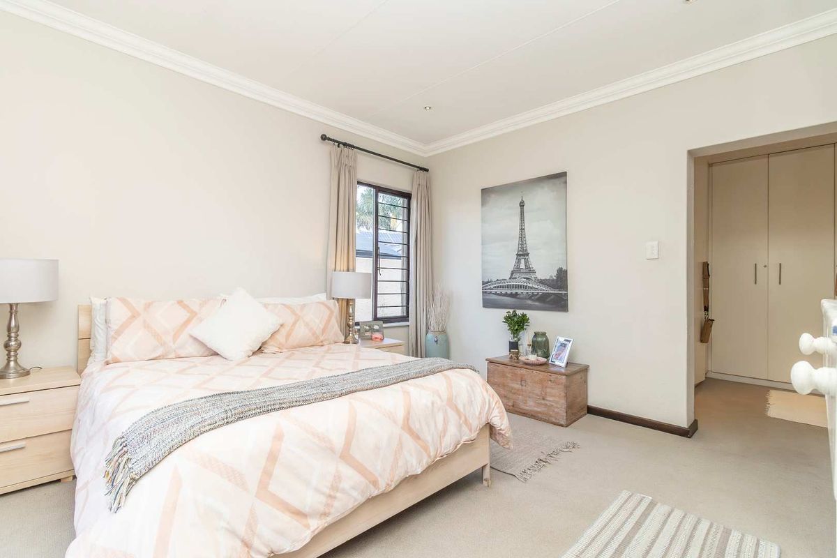 A well-maintained bedroom featuring neutral carpeting, crown molding, and built-in cupboards in the adjacent dressing area.