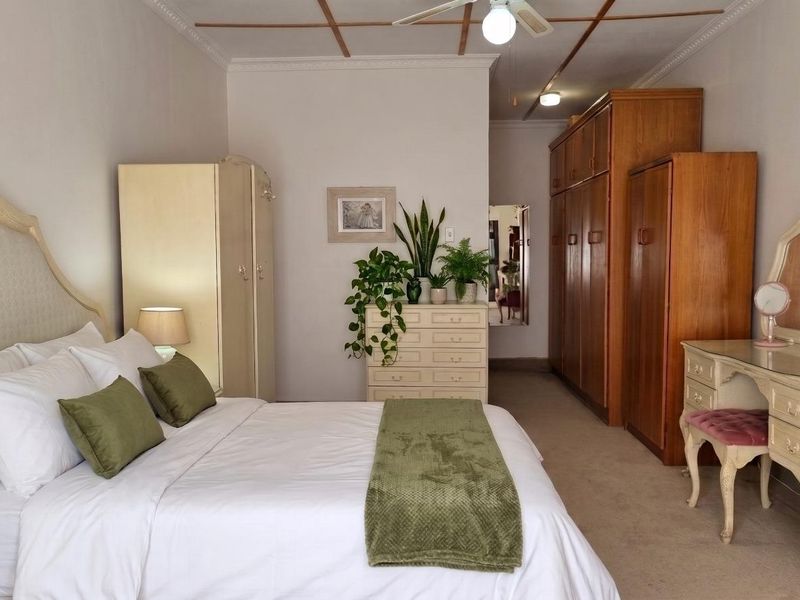 Spacious bedroom featuring built-in wooden cupboards, ceiling fan, and decorative coved cornicing, offering a traditional aesthetic with ample storage space.