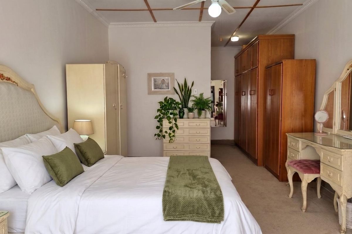 Spacious bedroom featuring built-in wooden cupboards, ceiling fan, and decorative coved cornicing, offering a traditional aesthetic with ample storage space.