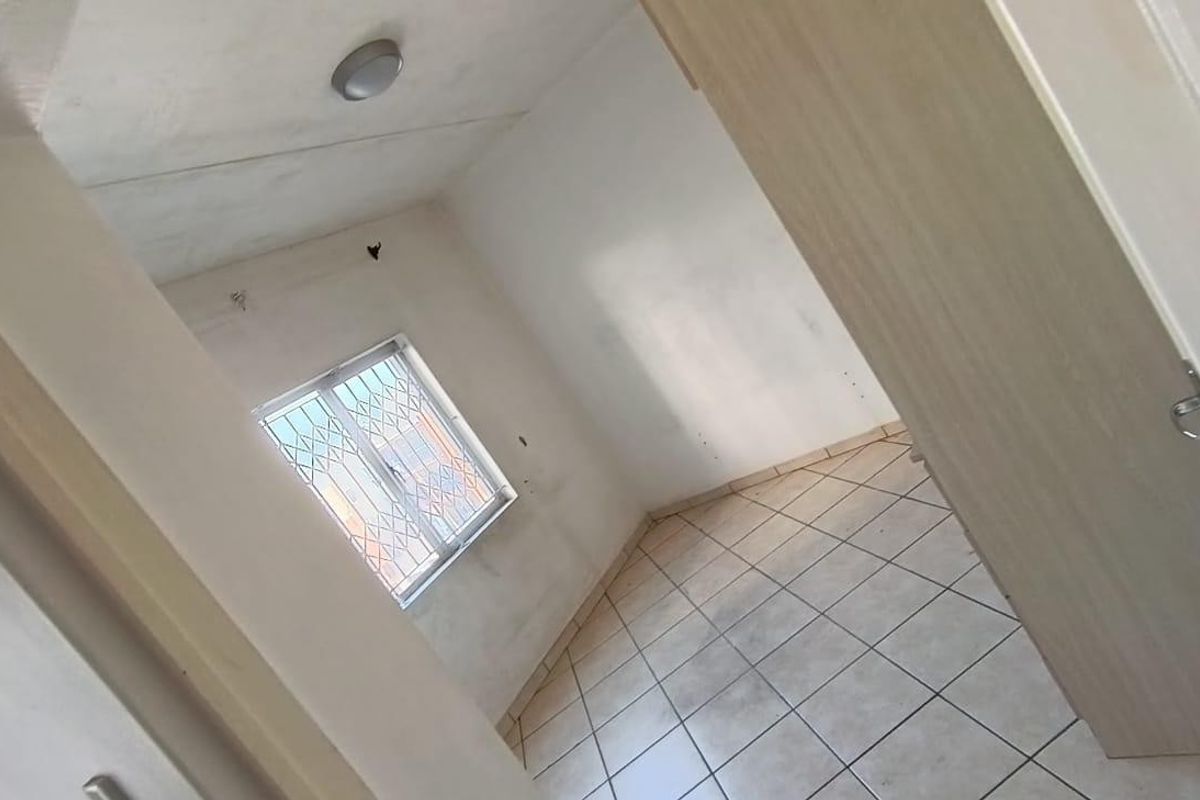 An empty bedroom featuring tiled flooring, a window with security bars, and a built-in cupboard, requiring cosmetic updates to the walls and ceiling.
