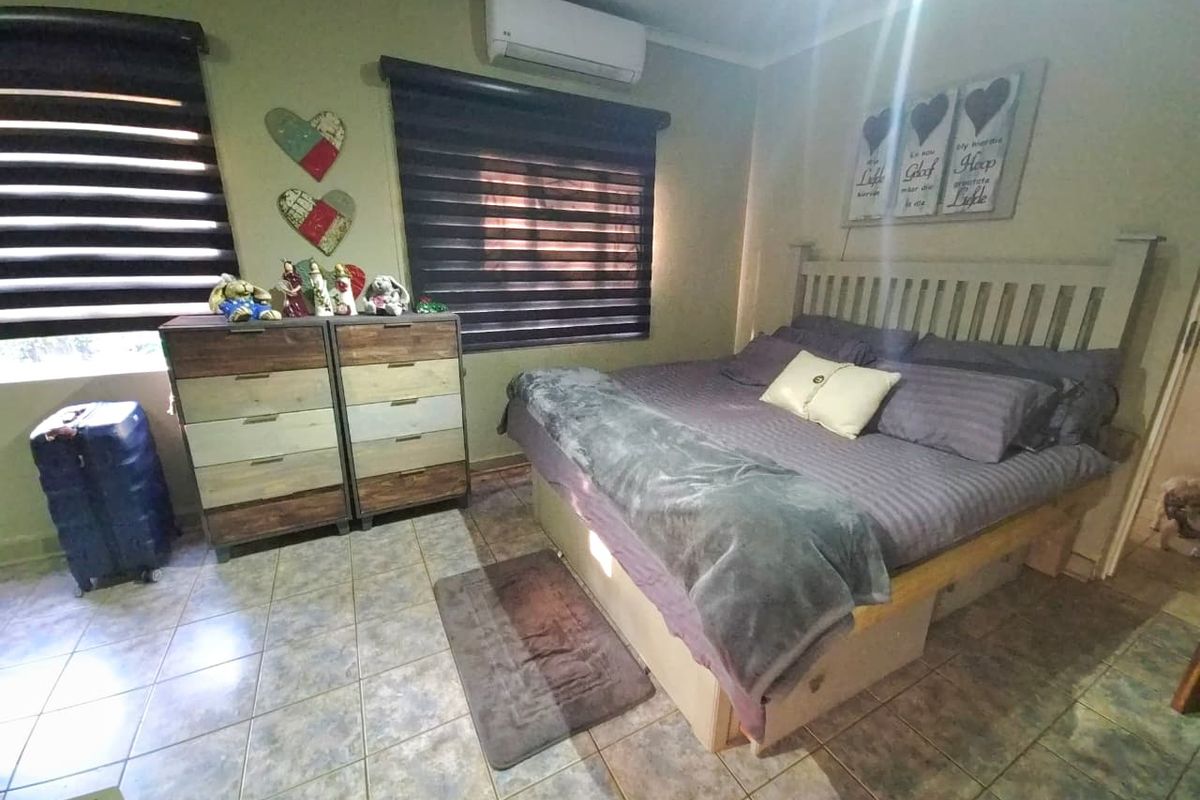 A bedroom featuring tiled flooring, roller blinds, and a wall-mounted split-system air conditioner.