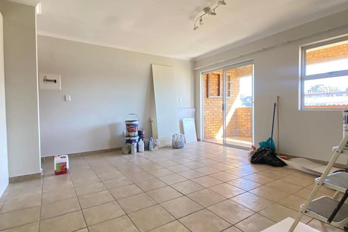 An empty, tiled living area featuring a sliding glass door leading to an outdoor space, currently undergoing minor maintenance and painting.