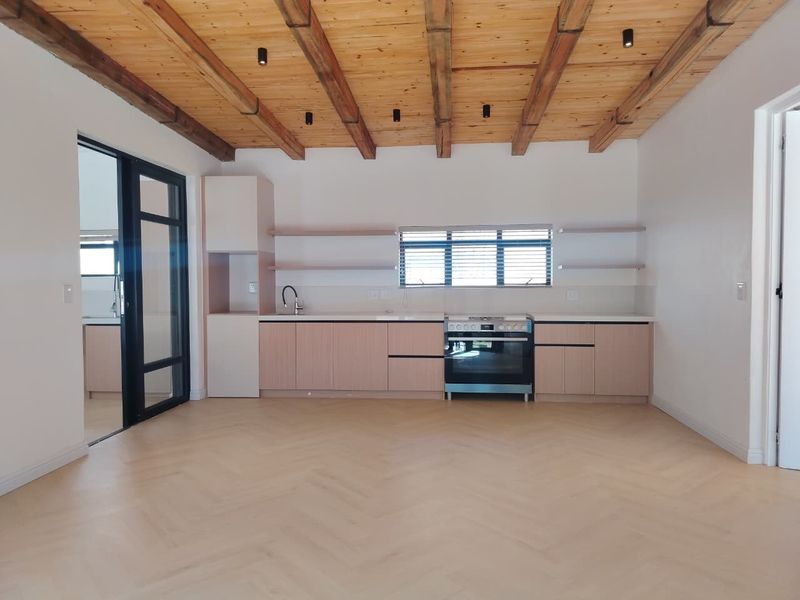 Modern kitchen featuring light wood cabinetry, herringbone flooring, and exposed timber ceiling beams, complemented by a sleek black-framed glass door.