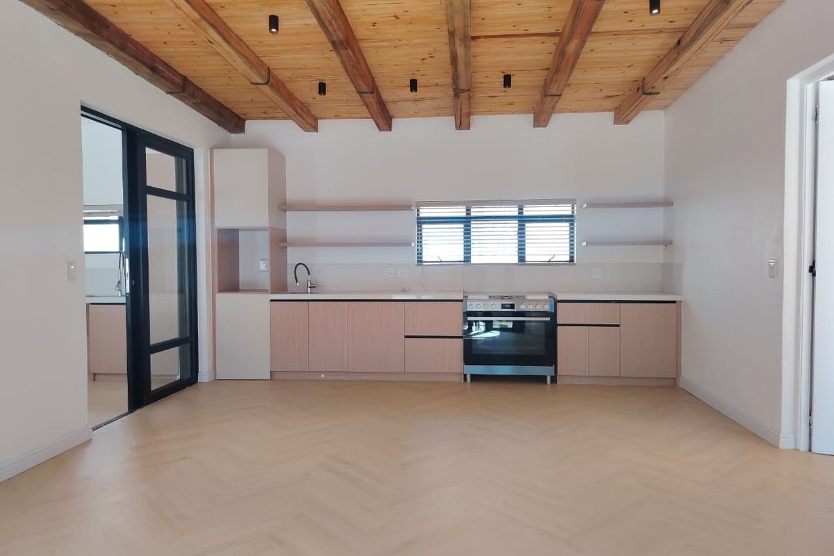 Modern kitchen featuring light wood cabinetry, herringbone flooring, and exposed timber ceiling beams, complemented by a sleek black-framed glass door.
