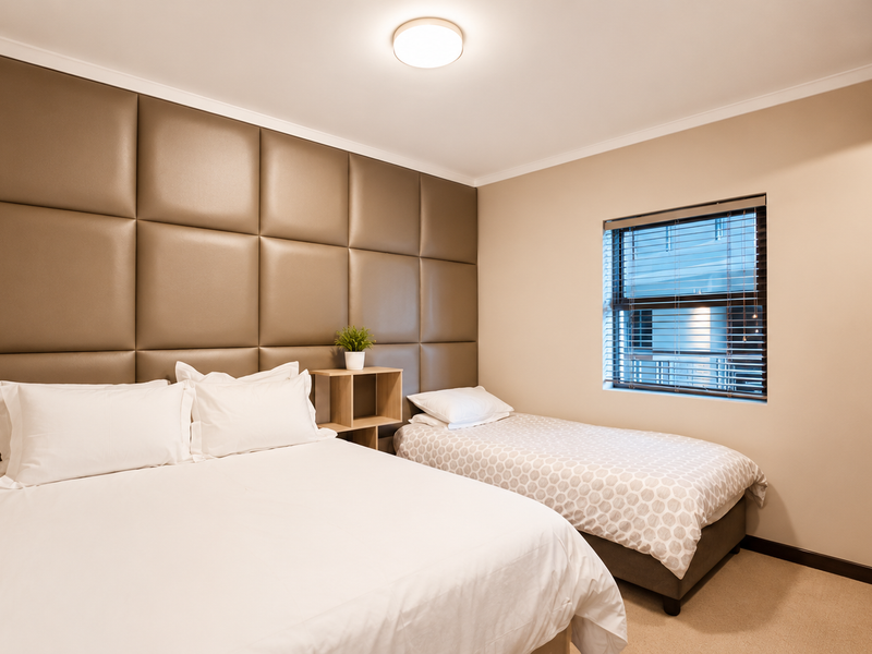 A well-maintained bedroom featuring custom upholstered wall paneling, built-in wardrobe storage, and neutral carpeting.