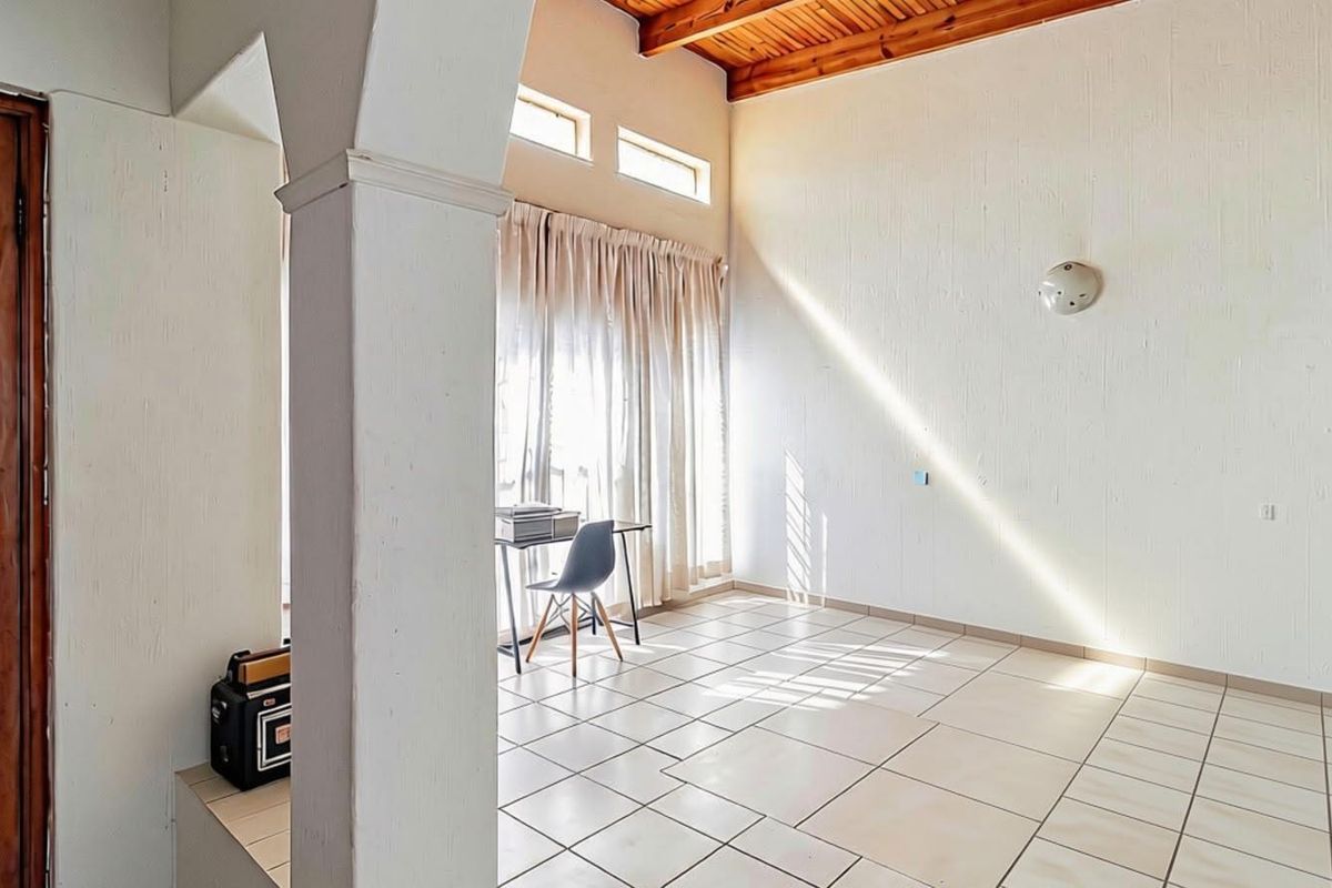 Spacious living area featuring high ceilings with exposed timber beams, tiled flooring, and an architectural archway leading to an adjacent space.