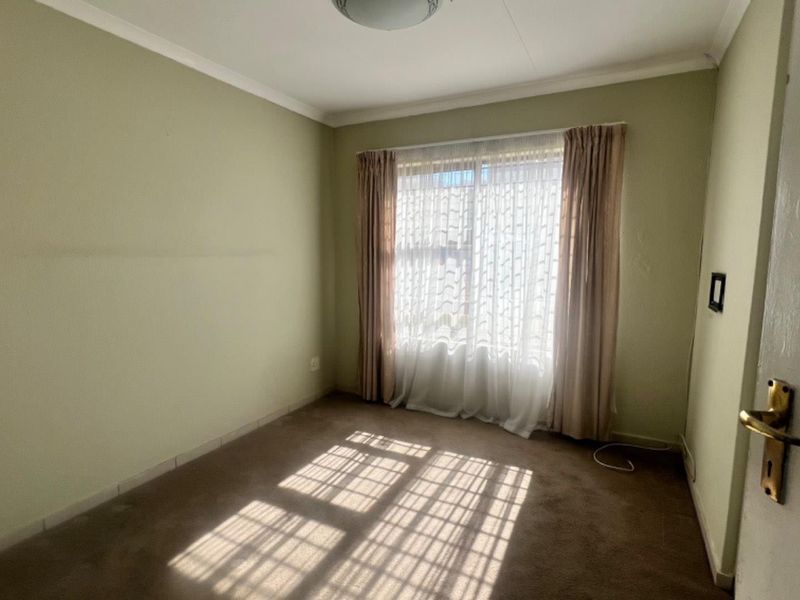 A vacant bedroom featuring neutral wall paint, carpet flooring, and natural light through a window with curtains.