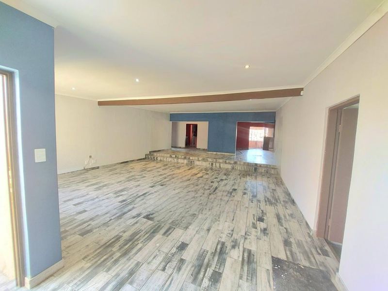 Spacious open-plan living area featuring a raised platform, modern wood-look floor tiles, and recessed downlighting throughout the interior space.