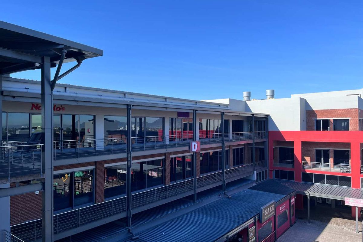 A modern multi-level commercial office complex featuring glass facades, steel balcony railings, and a paved courtyard area.