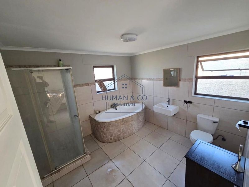 A spacious bathroom featuring a built-in bathtub, separate shower enclosure, wall-mounted basin, and toilet with neutral tiled finishes throughout.