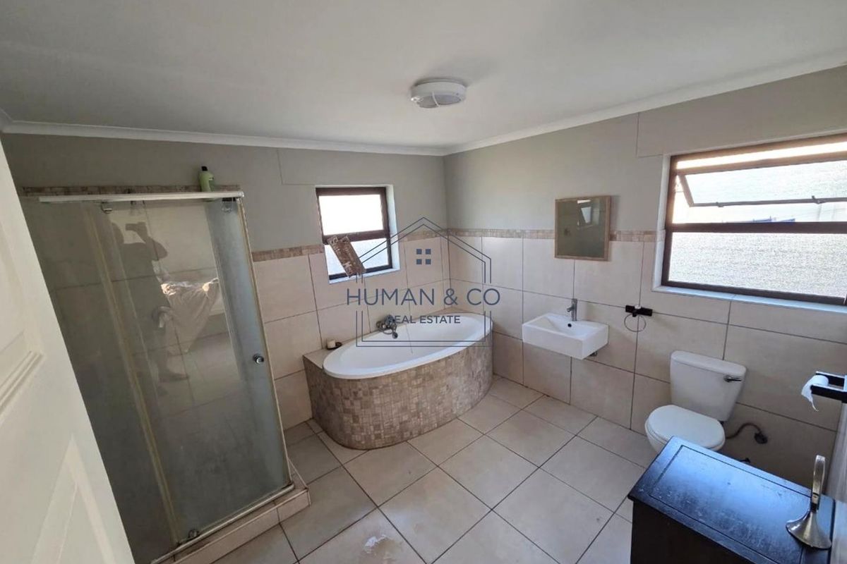 A spacious bathroom featuring a built-in bathtub, separate shower enclosure, wall-mounted basin, and toilet with neutral tiled finishes throughout.