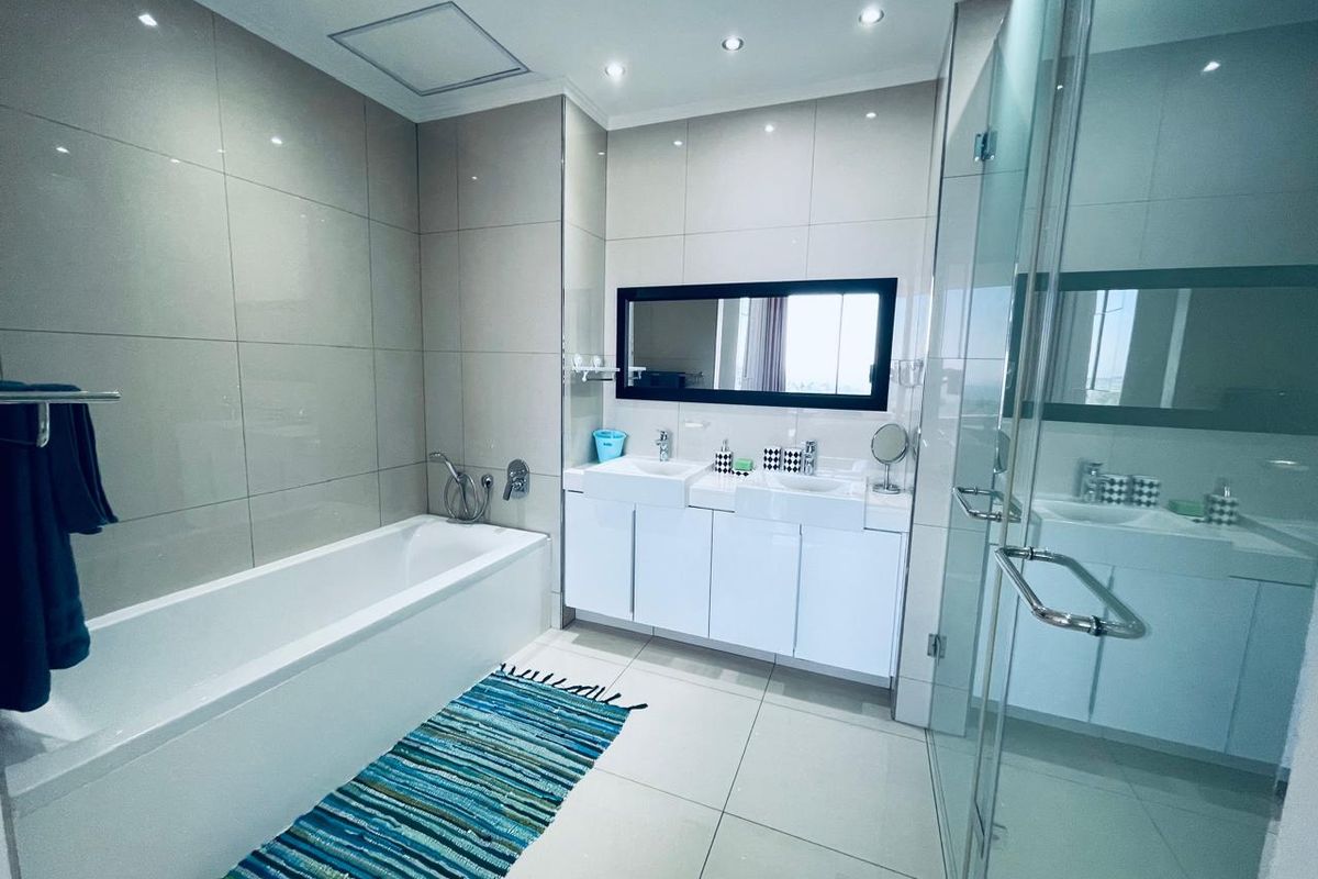 Modern bathroom featuring a double vanity, bathtub, and a separate glass-enclosed shower with neutral wall and floor tiling.