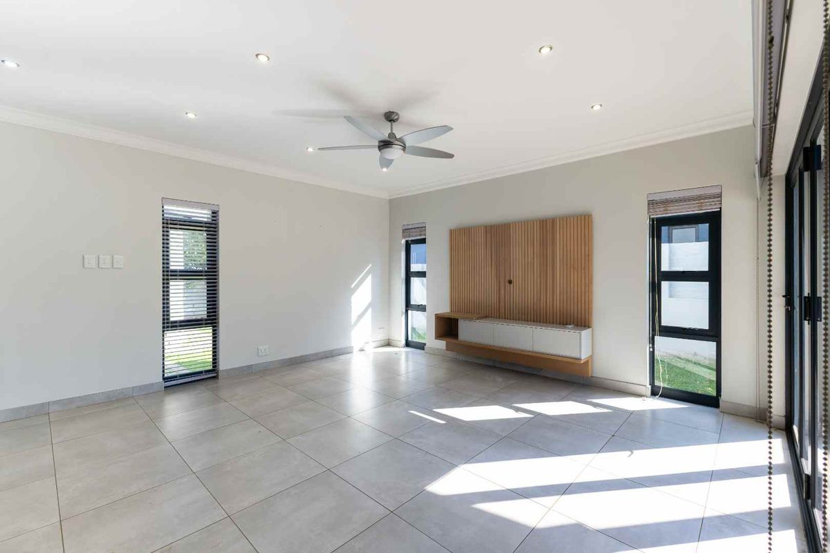 Spacious, light-filled living room featuring large format floor tiles, a modern built-in media console with timber detailing, and direct access to the outdoor area.