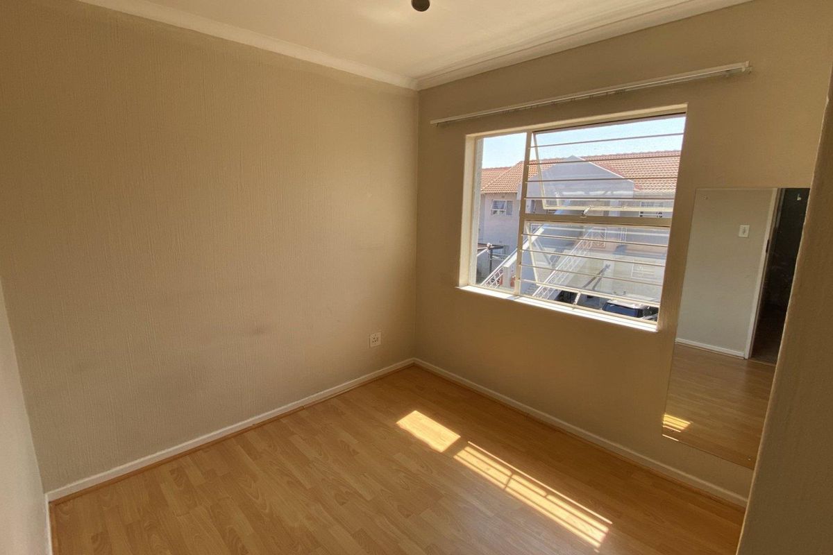 An empty bedroom featuring laminate flooring, neutral walls, and a large window with louvre panes, offering a blank canvas for personalization.