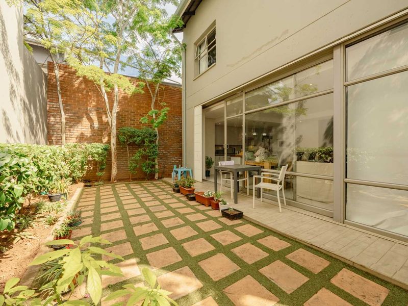 A private rear courtyard featuring a paved patio area, landscaped garden, and large sliding glass doors providing seamless indoor-outdoor flow.