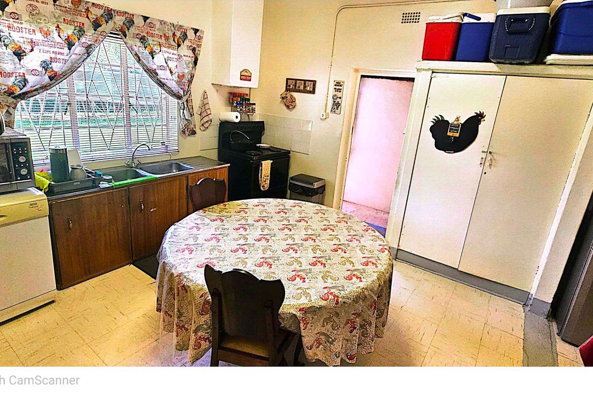 A dated kitchen featuring basic cabinetry, a freestanding stove, and a small dining area with vinyl flooring.