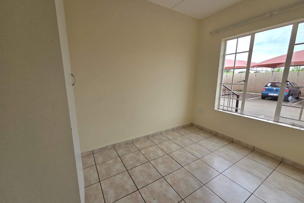 A bright, empty bedroom featuring neutral tiled flooring and a large window with views of the parking area.