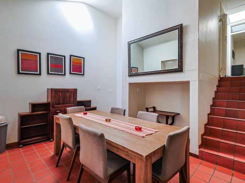 Dining area featuring terracotta floor tiles, a high ceiling with a skylight, and a built-in staircase leading to the upper level.