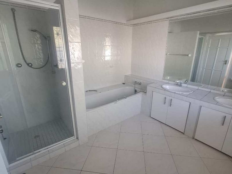 A spacious bathroom featuring a separate shower enclosure, built-in bathtub, and a double vanity unit with tiled flooring and wall-to-wall mirror.