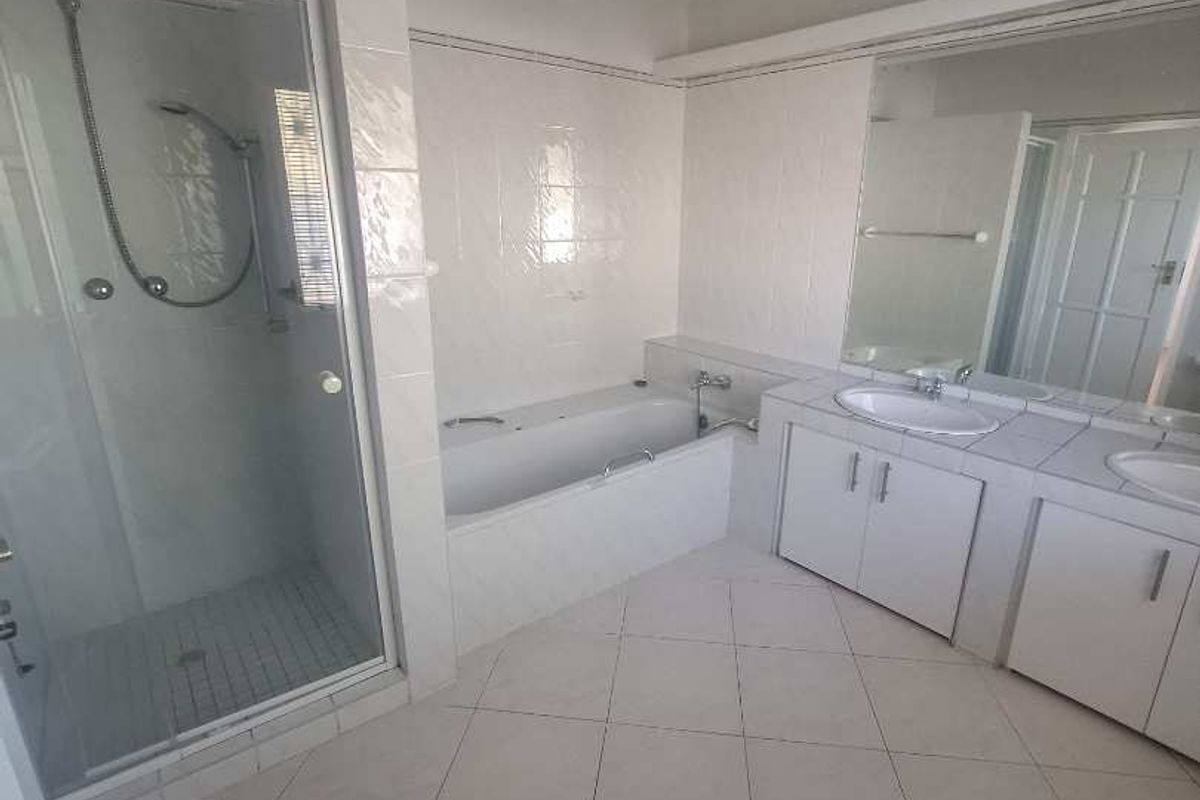 A spacious bathroom featuring a separate shower enclosure, built-in bathtub, and a double vanity unit with tiled flooring and wall-to-wall mirror.