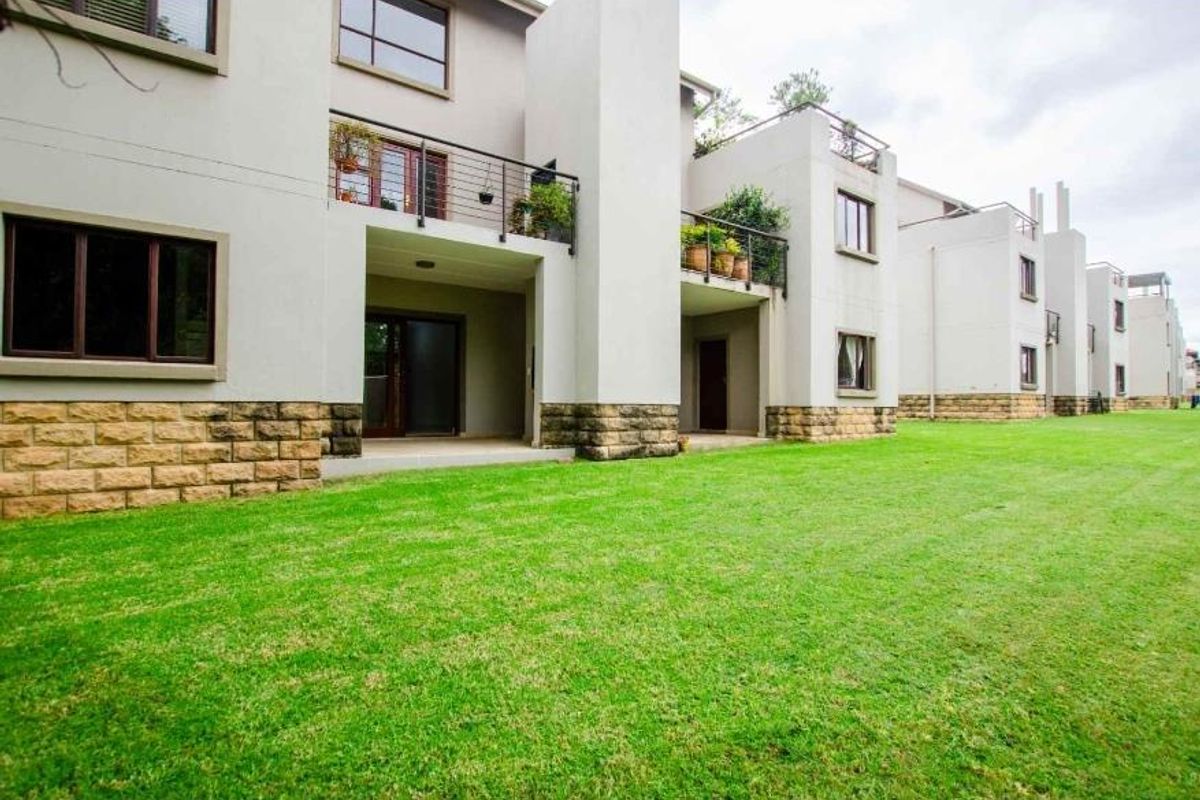 Rear view of a modern apartment complex featuring stone-clad lower walls, private balconies, and a well-maintained communal lawn area.