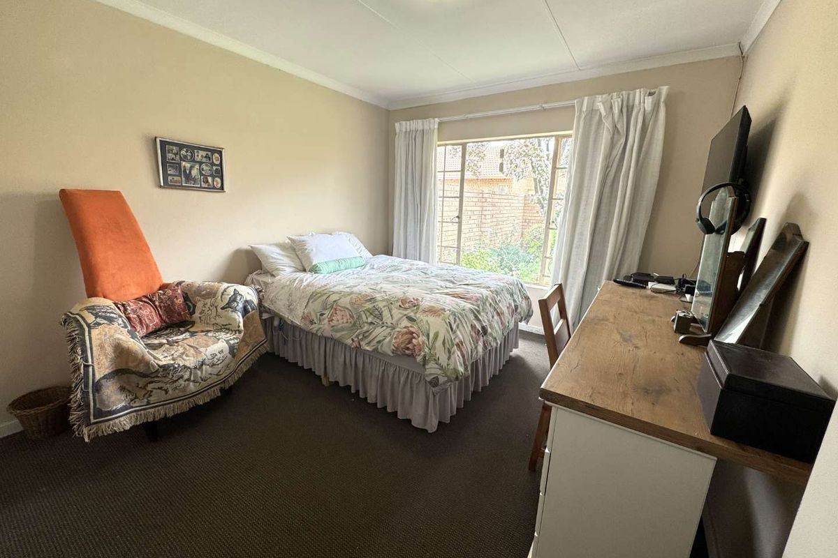 A standard bedroom featuring neutral wall tones, carpeted flooring, and a large window providing natural light and garden views.