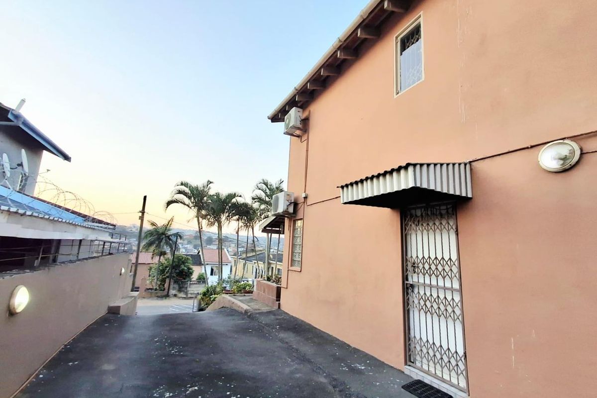 Exterior view of the property side featuring an asphalt driveway, security gate, and wall-mounted air conditioning unit.
