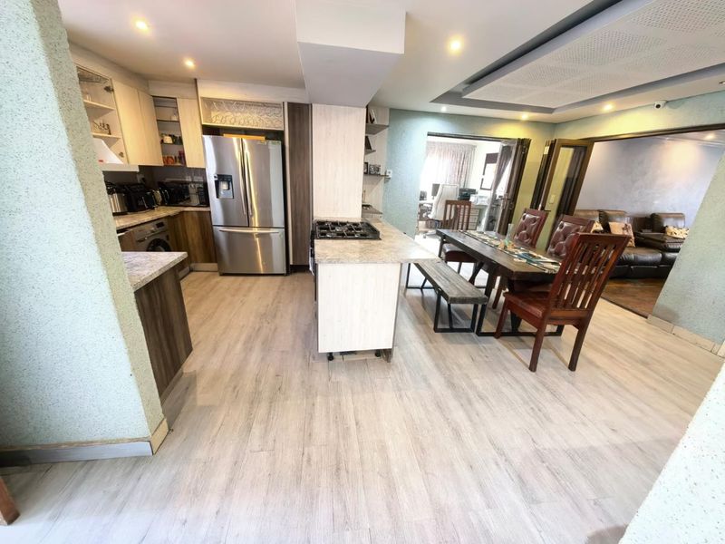 Open-plan kitchen and dining area featuring modern cabinetry, granite countertops, a central gas hob island, and light-toned laminate flooring throughout.