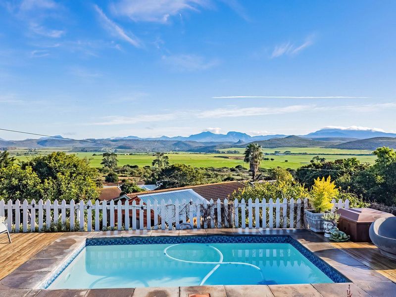 Outdoor pool area featuring timber decking and a picket fence, offering expansive scenic views of the surrounding landscape and mountains.