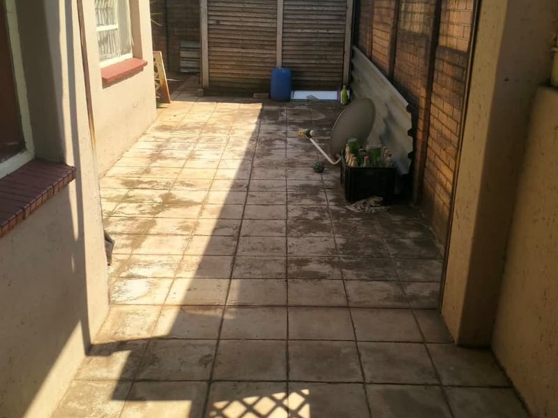 A narrow rear exterior area featuring tiled paving, a brick boundary wall, and a corrugated metal storage shed.