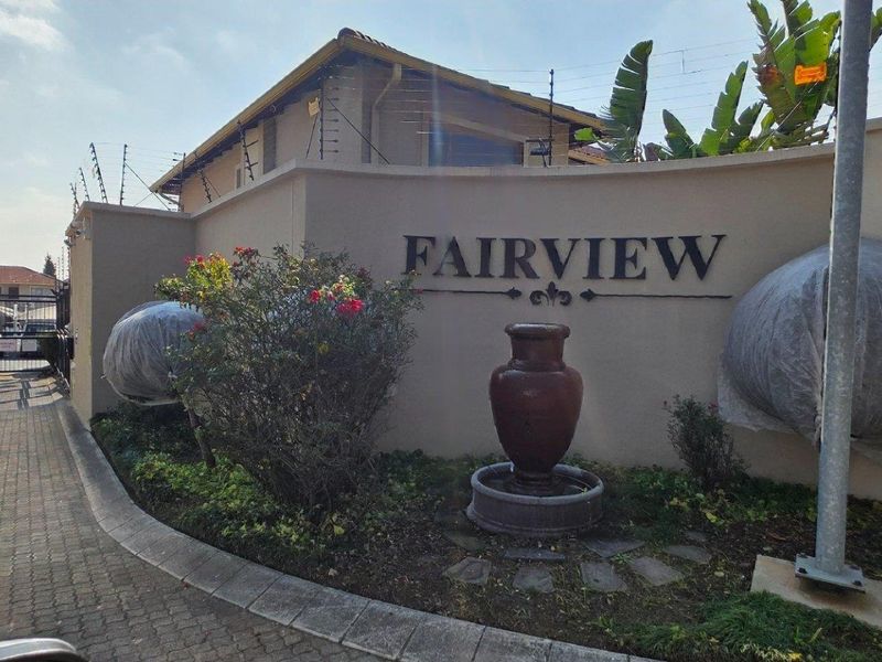 Entrance view of Fairview complex featuring a secure gated access point, boundary wall with electric fencing, and a decorative water feature.