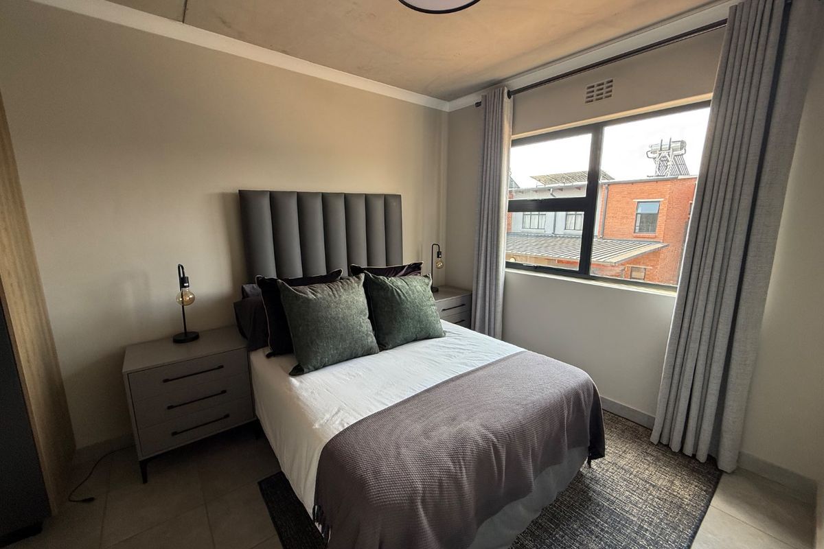 A well-maintained bedroom featuring tiled flooring, neutral walls, and an aluminium-framed window with curtains.