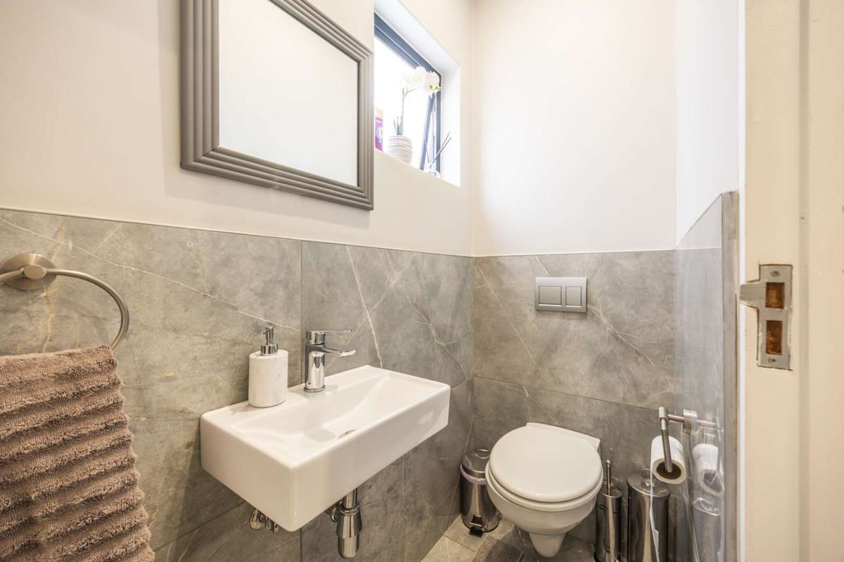 A compact guest bathroom featuring modern grey marble-look wall tiles, a wall-mounted basin, and a sleek wall-hung toilet with a concealed cistern.
