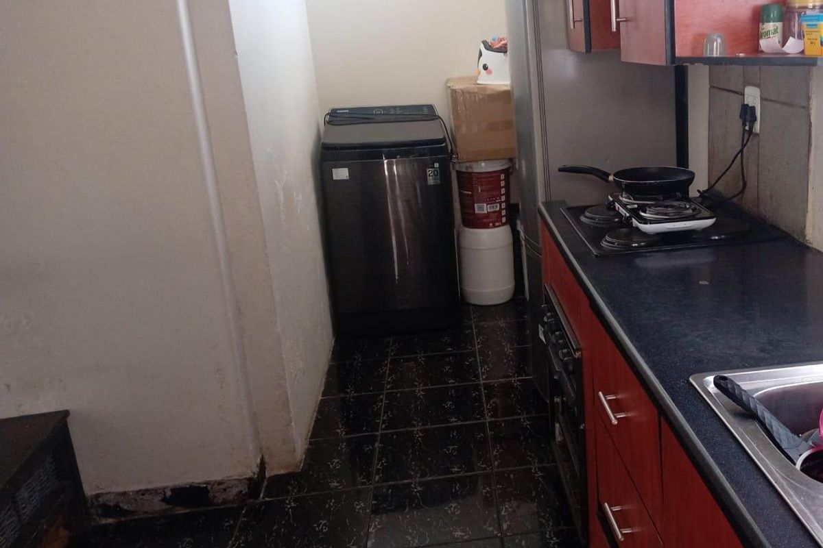A compact kitchen area featuring dark cabinetry, a built-in oven and hob, stainless steel sink, and dedicated space for a washing machine.