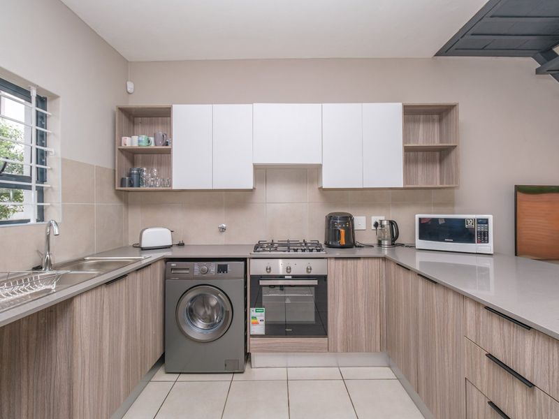 Modern kitchen featuring wood-grain cabinetry, stone countertops, gas hob, built-in oven, and integrated laundry plumbing, finished with neutral tiled splashbacks and flooring.