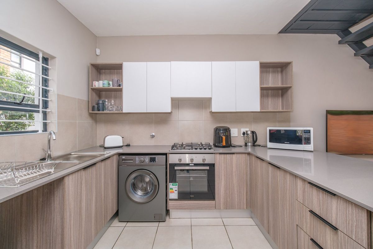 Modern kitchen featuring wood-grain cabinetry, stone countertops, gas hob, built-in oven, and integrated laundry plumbing, finished with neutral tiled splashbacks and flooring.