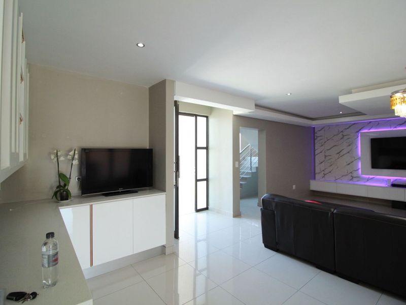 Modern open-plan living area featuring polished porcelain tiles, a sophisticated built-in media wall with marble-effect cladding, and integrated LED accent lighting.