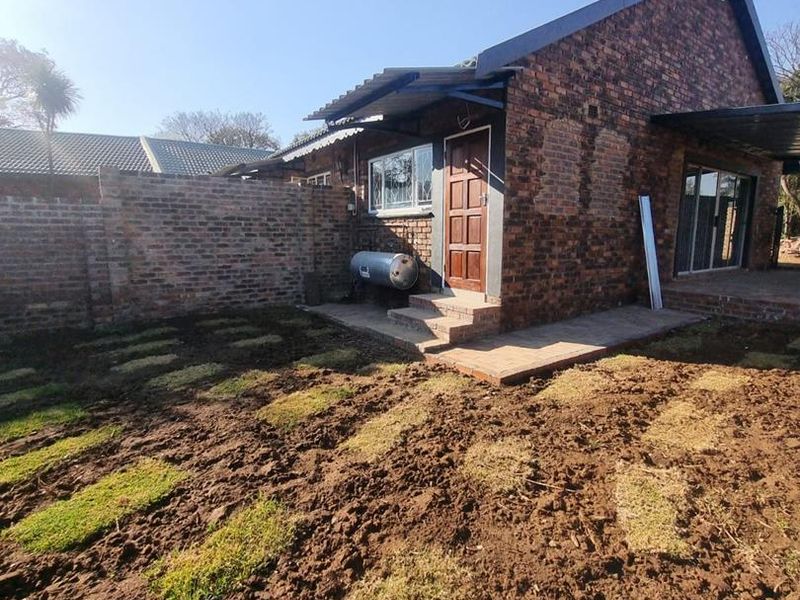 Rear view of a face brick house featuring a paved patio area, solar geyser, and a garden currently undergoing landscaping.