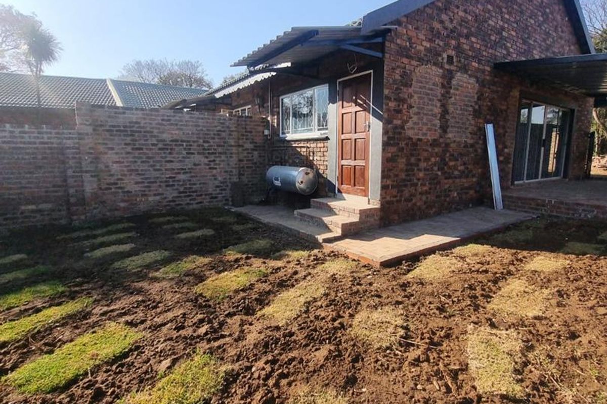 Rear view of a face brick house featuring a paved patio area, solar geyser, and a garden currently undergoing landscaping.