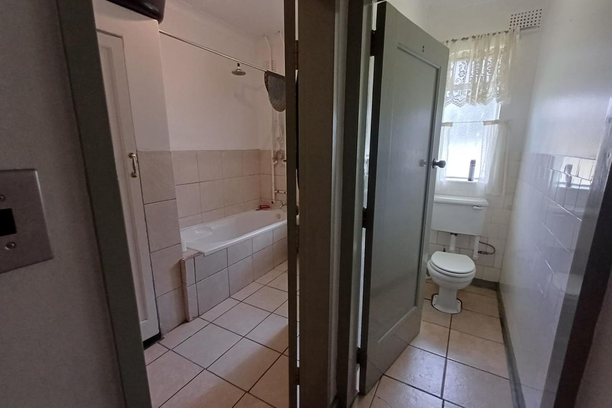 A functional bathroom featuring a built-in bathtub with shower head and a separate toilet area with tiled finishes throughout.