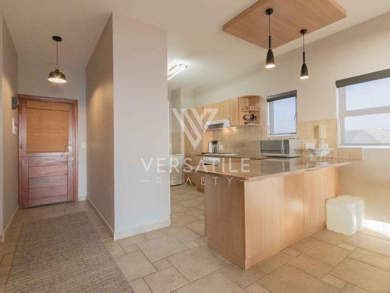 Open plan kitchen and entrance area featuring light wood cabinetry, tiled flooring, and modern pendant lighting in a well-maintained apartment setting.