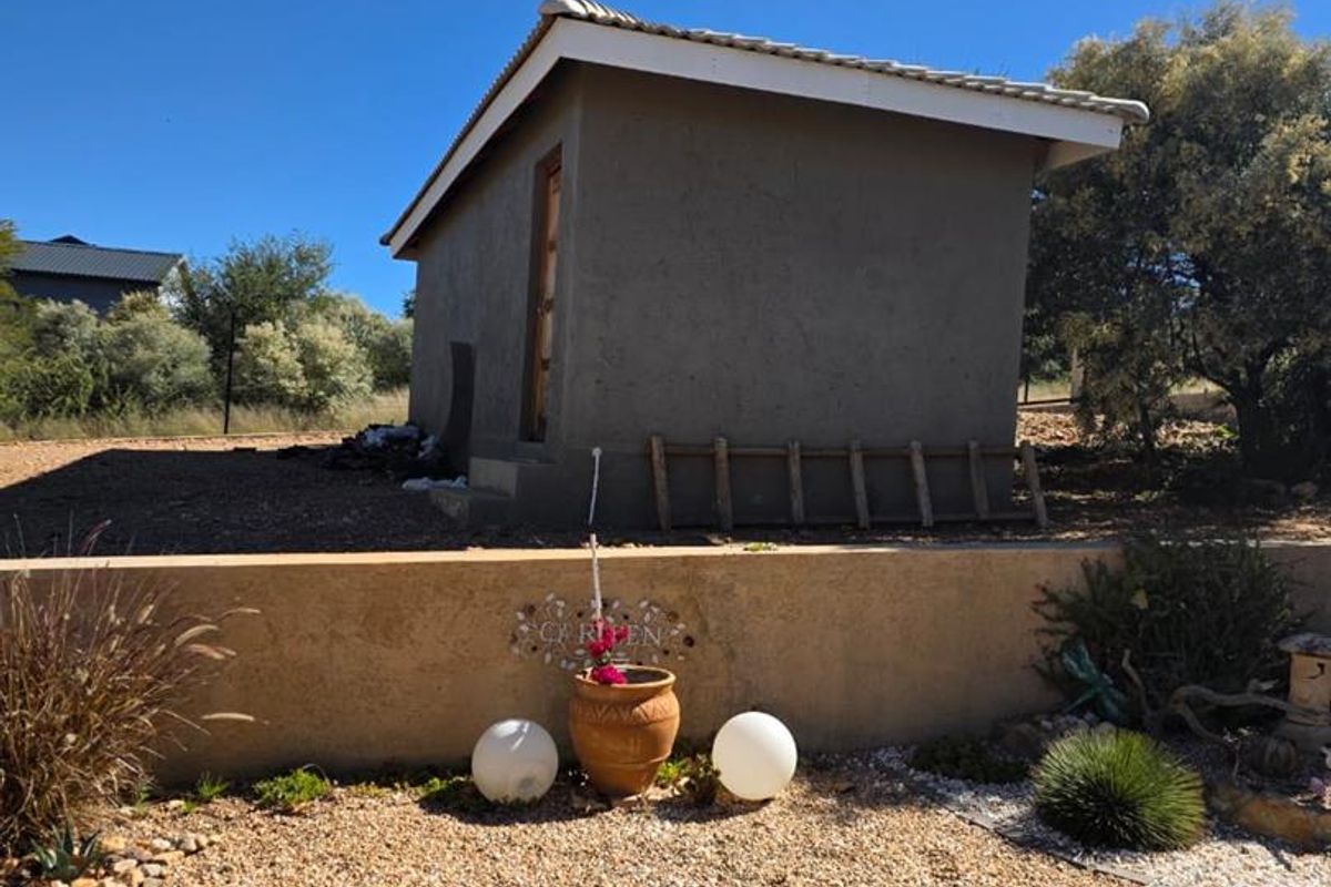 A detached outbuilding or utility structure situated in a landscaped garden area with gravel surfacing and a low retaining wall.