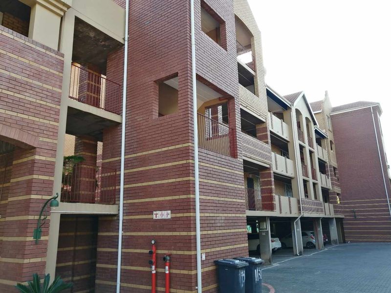 Exterior view of a multi-story apartment complex featuring face brick construction, covered parking bays, and private balconies.