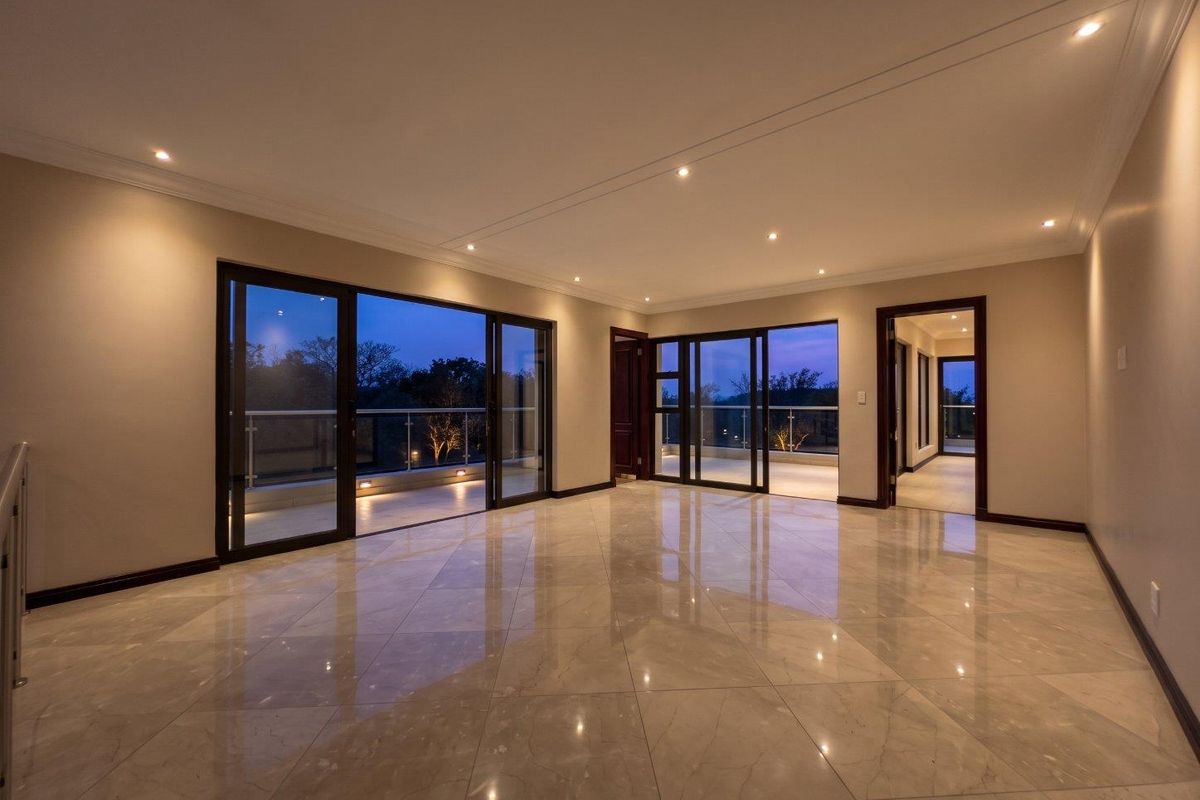 Spacious, modern living area featuring polished porcelain tiles, recessed lighting, and large sliding glass doors opening onto a balcony with a glass balustrade.