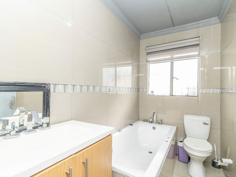 A well-maintained bathroom featuring full-height wall tiling, a built-in vanity unit, a bathtub, and a standard toilet.