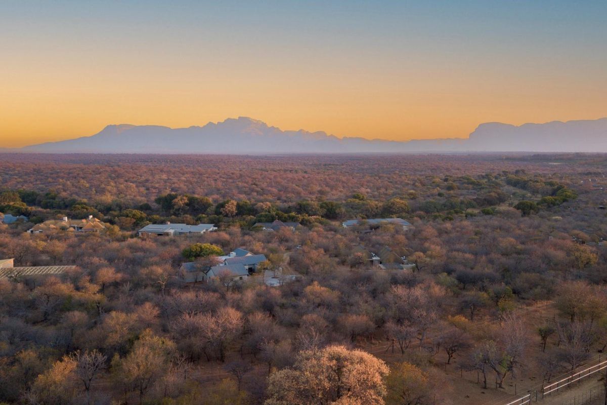 An expansive aerial view of a bushveld estate featuring scattered residential dwellings set against a scenic mountain range at sunset.