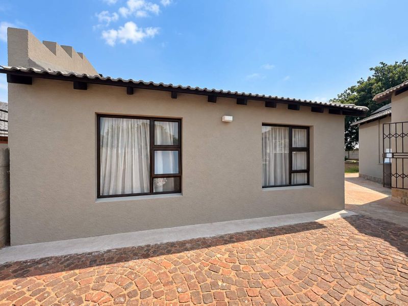 A well-maintained cottage exterior featuring a tiled roof with exposed rafters, modern aluminium window frames, and neat cobblestone paving.