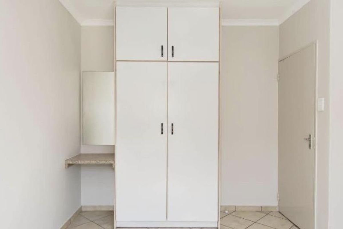 A clean bedroom interior featuring a white built-in wardrobe with overhead storage and an integrated vanity shelf, finished with neutral tiled flooring.