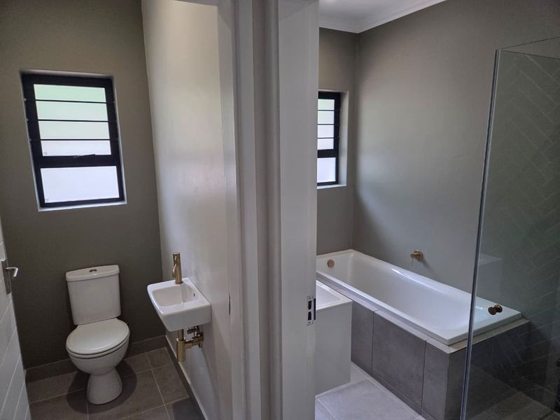 Modern bathroom featuring a separate toilet area with wall-mounted basin and a main bathroom area with a bathtub and glass shower screen.