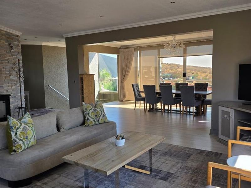 Spacious open-plan living and dining area featuring a stone-clad fireplace, recessed lighting, and large glass doors leading to an outdoor view.